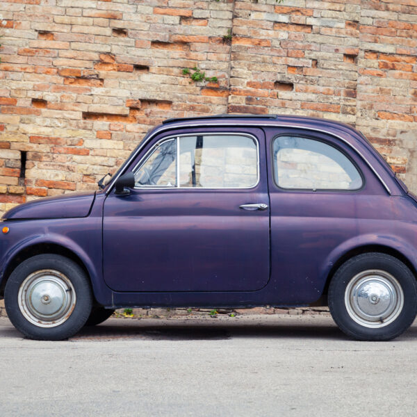 This image shows a vintage Fiat 500 parked in front of a brick wall. Fiat 500 tours in Italy are among the best classic car tours in Europe.