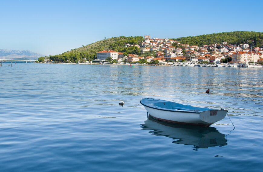 This image shows a small boat in the calm sea, with a red-rooftoped town in the background.